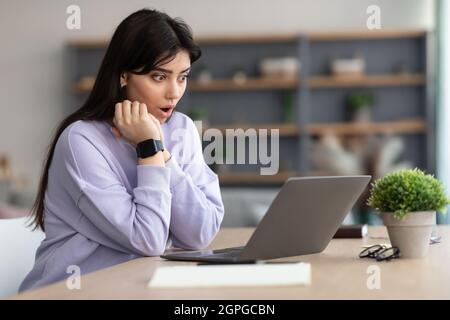 Überraschte Frau, die am Schreibtisch saß und einen Laptop benutzte Stockfoto