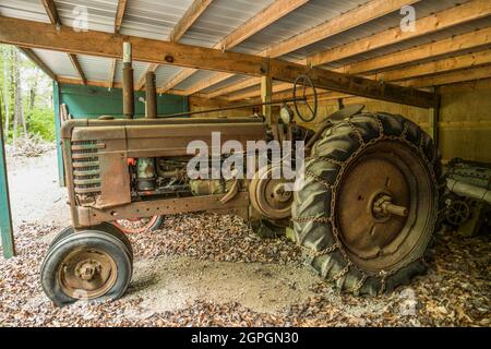 Großer verrosteter Vintage-Traktor, der in einem offenen Schuppen sitzt, mit nicht mehr verwendeten Platten, weggeworfenen und vergessenen Nahaufgangsansicht Stockfoto