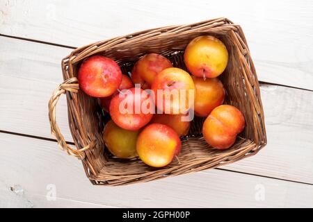 Mehrere saftige, süße gelb-rote Pflaumen in einem Korb auf einem Holztisch, Nahaufnahme, Draufsicht. Stockfoto