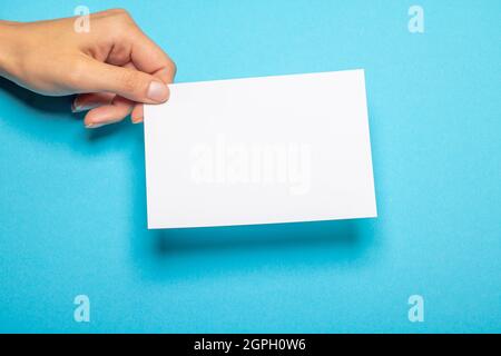 Weibliche Hand hält ein leeres Stück Papier mit Kopierraum vor einem hellblauen Hintergrund Stockfoto