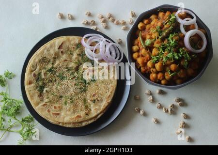 Perfekt runder Paratha. Indisches Fladenbrot aus Weizenmehl, gekrönt mit Sesamsamen und Korianderblättern, serviert mit weißer Kichererbsengravur Stockfoto