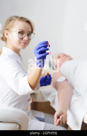 Lächelnder Arzt in Latexhandschuhen mit Reagenzglas. Bluttest aus der Handvene Stockfoto