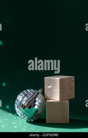 Stillleben mit Holzwürfeln und Diskokugel, die Sonneneruptionen vor smaragdgrünem Hintergrund reflektiert Stockfoto