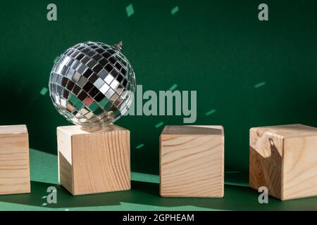 Stillleben mit Holzwürfeln und Diskokugel, die Sonneneruptionen vor smaragdgrünem Hintergrund reflektiert Stockfoto