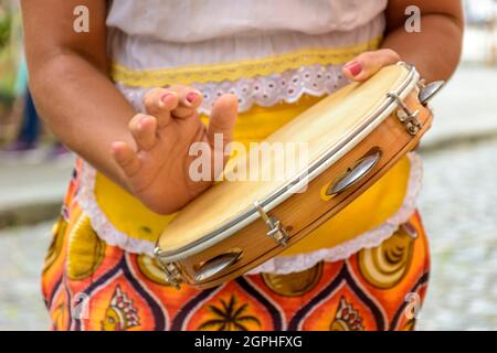 Junge Frau in farbenfrohen Kleidern spielt Tamburin während einer Samba-Aufführung in Salvador, Bahia. Stockfoto