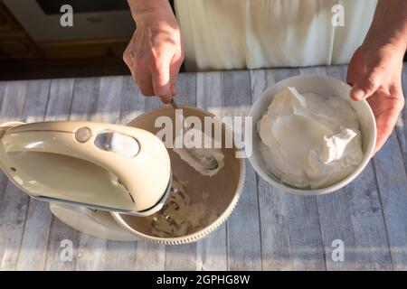 Schritt für Schritt der Prozess der Herstellung von saurer Creme. Frauenhänden geben saure Creme zum Schlagen in die Rührschüssel. Stockfoto