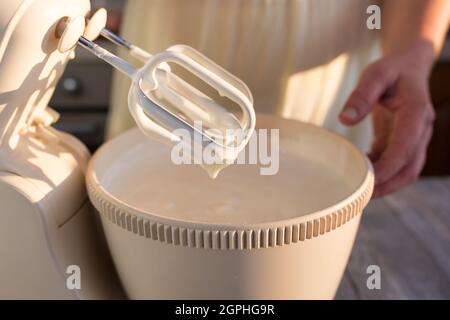 Schritt für Schritt der Prozess der Herstellung von saurer Creme. Die Creme ist fertig. Die Hostess entfernt die Rührbesen mit der fertigen Creme aus dem Behälter. Stockfoto