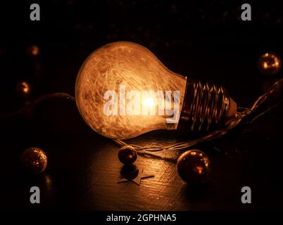 Nahaufnahme einer Glühbirne mit winzigen weißen Features, die auf einer dunklen Oberfläche mit goldenen Glitzerkugeln liegen Stockfoto