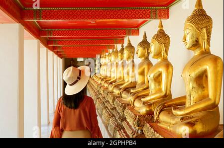 Weibliche Besucher des Klosters mit einer großen Gruppe sitzender Buddha-Bilder im Wat Pho oder Tempel des Reclining Buddha, Bangkok Old City, Thailand Stockfoto