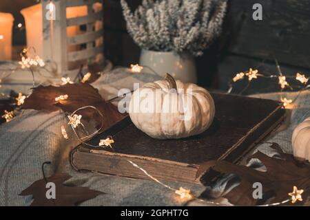 Herbstdekoration mit weißem Kürbis, Lichtern und getrockneten Blättern auf der Veranda in der Nacht Stockfoto