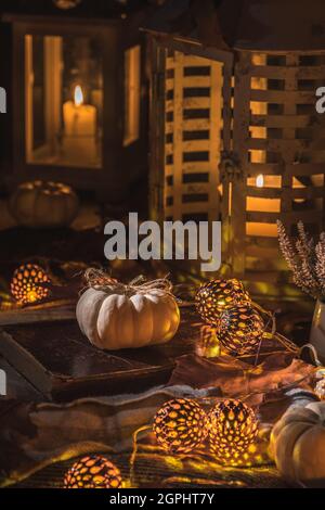 Herbstdekoration mit weißen Kürbissen, Lichtern, Decke und getrockneten Blättern auf einer Terrasse oder Terrasse in der Nacht, vertikales Stockfoto Stockfoto