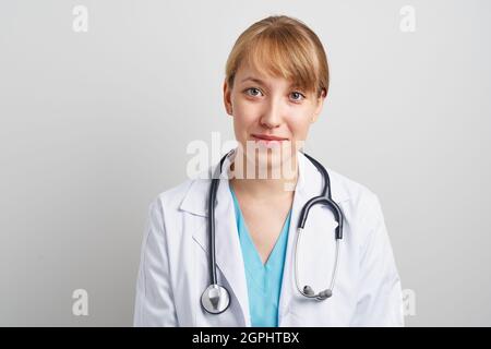 Junge, vertrauenswürdige Ärztin mit Phonendoskop und weißem Mantel, die auf die Kamera schaut Stockfoto