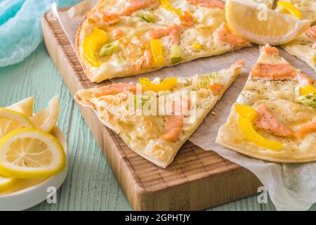 Flambienstücke mit Lachs, gelbem Pfeffer und Frühlingszwiebeln auf einem Holzbrett auf hellgrünem Hintergrund Stockfoto