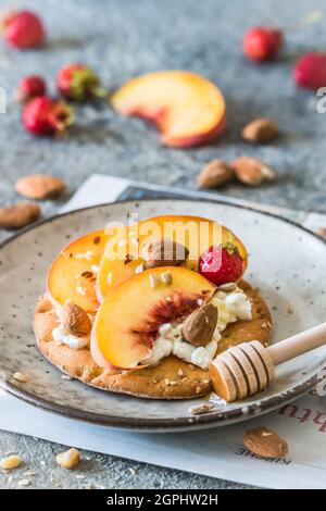 Runde Crispbread-Scheibe mit körnigem Frischkäse und frischen Pfirsichen, gesundes Frühstück, vertikal. Stockfoto