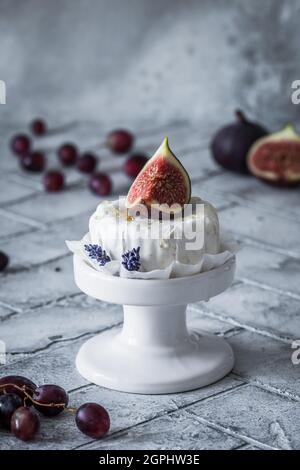 Ganzer runder Weichkäse mit Honig und Feige auf grauen Fliesen, senkrecht Stockfoto