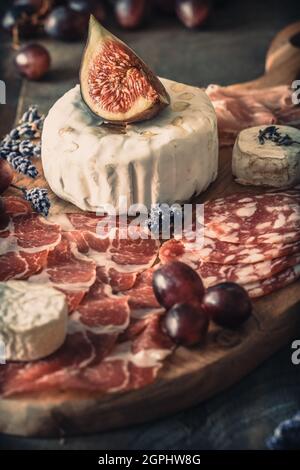 Verschiedene geräucherte Wurst Spezialitäten und ein weicher Käse auf einem Holzbrett, mit Feigen und Trauben geschmückt, konzentrieren sich auf den Käse, vertikal Stockfoto