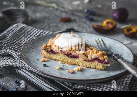 Pflaumenkuchen mit gerösteten Mandeln und Creme fraiche auf einem grauen Teller auf grauem Hintergrund Stockfoto