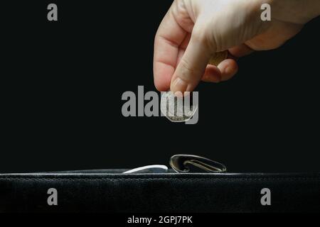 Die Hand einer unsichtbaren Frau legt eine Münze in eine Brieftasche Stockfoto