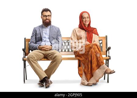 Bärtiger Mann und eine Frau in einem Hijab, die auf einer Bank sitzen und isoliert auf weißem Hintergrund die Kamera betrachten Stockfoto