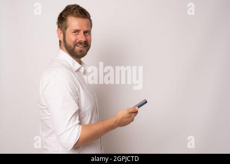 Profilseitenfoto des positiven fröhlichen Mannes, der sein Mobiltelefon auf weißem Hintergrund hält. Stockfoto