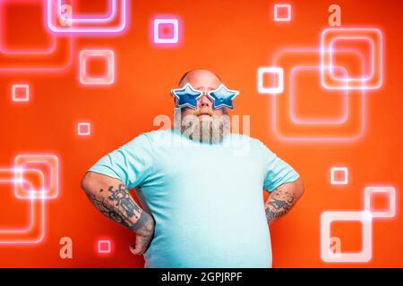 Ein fetter, nachdenklicher Mann mit Bart, Tattoos und Sonnenbrille ist bereit, Musik zu tanzen Stockfoto