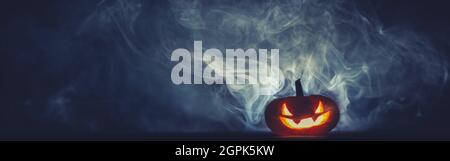 Gruselig geschnitzte Jack o Lantern glühend rot in dichtem Rauch in der Nacht. Halloween Hintergrund mit Platz für Text. Stockfoto