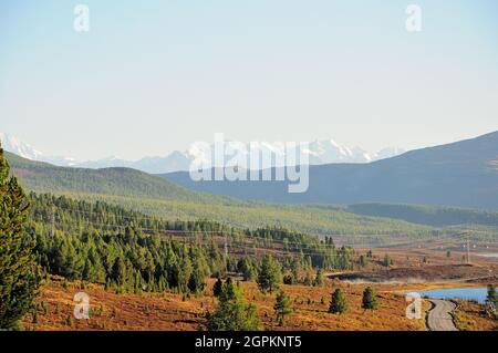 Ein Blick auf die mit Nadelwäldern überwuchert Bergtaiga, einem Straßenfragment und einer elektrischen Übertragungsleitung, die vorbeiführt und schneebedeckt ist Stockfoto