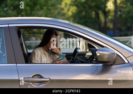 Weinendes junges Mädchen las Nachricht auf dem Handy. Frustriert verärgert junge Frau am Fahrersitz im Auto Stockfoto