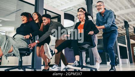 Spielzeit im Büro. Fröhliche Gruppe von Geschäftsleuten, die sich an einem modernen Arbeitsplatz auf Stühlen schieben. Gruppe von erfolgreichen Geschäftsleuten mit Stockfoto