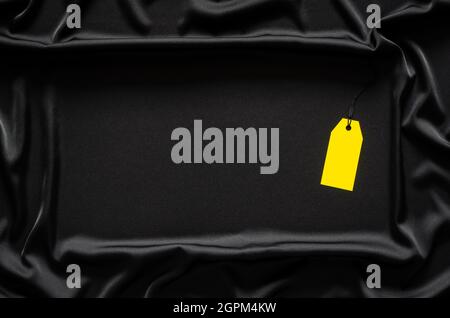 Ein gelbes, leeres Preisschild auf schwarzem, glattem und welligen Tuch mit Platz für Text. Black Friday Konzept. Stockfoto