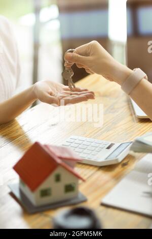 Nahaufnahme eines Immobilienmaklers, der einem neuen Mieter einen Hausschlüssel übergibt, nachdem er eine Mietkaution erhalten hat. Stockfoto