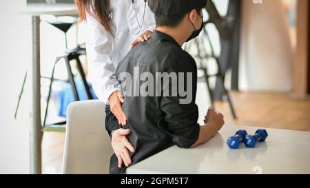 Ein männlicher Patient kommt in die Therapieklinik und klagt über Rückenschmerzen. Der Therapeut untersucht die körperlichen Schmerzen des Patienten im Untersuchungsraum Stockfoto