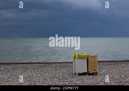 Eine Packung Plastikliegen an einem einsamen Strand am Meer. Schließung der Strandsaison. Es gibt dunkle Wolken am Himmel. Stockfoto