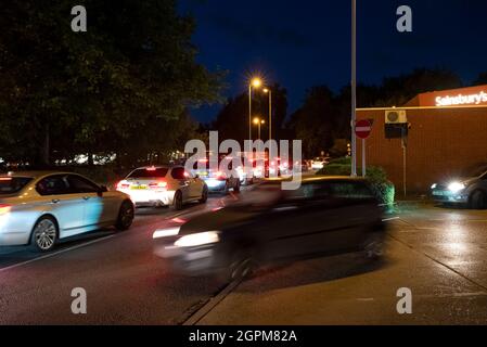 Apsley, Hertfordshire, Großbritannien. September 2021. Am frühen Abend im Dunkeln stehen die Autofahrer an der Tankstelle Apsley von Sainsbury an, um sich zu füllen. Autos, die sich mit ihren Lichtern an der Zufahrtsstraße zum Apsley Mills Retail Park anstellen, die zur Tankstelle führt. Frühere Autofahrer hatten sich schon einige Zeit in der Schlange gestellt, bevor ein Tanker, der bleifreies E10-Benzin lieferte, seine Ladung abgab. Autofahrer beginnen nach dem Tanken zu gehen. Viele Tankstellen in Hertfordshire und den umliegenden Grafschaften wurden geschlossen. Kredit: Stephen Bell/Alamy Stockfoto