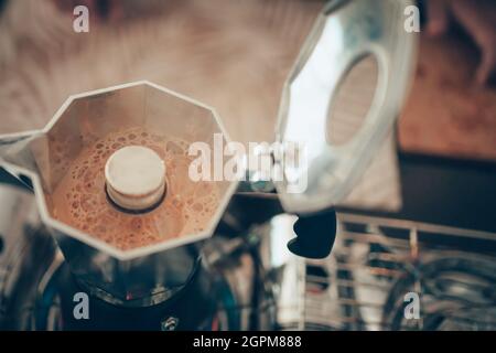 Brauen von schwarzem Moka-Kaffee mit der Moka-Kaffeemaschine und Kochen mit Rauch auf dem Gasherd. Stockfoto