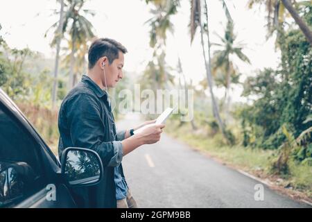 Ein Mann mit Wanderrucksack liest auf der Straße im Wald ein Kartenauto. Rucksack Reisekonzept. Stockfoto
