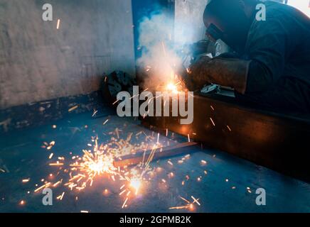 Schweißer schweißen Metall mit Argon-Lichtbogen-Schweißmaschine und hat Schweißfunken. Der Mann trägt eine Schweißmaske und Handschuhe. Sicherheit am Arbeitsplatz. Stockfoto