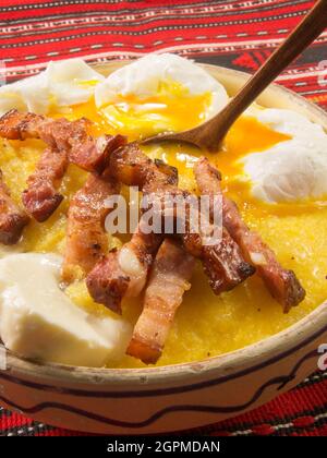 Polenta Bulz mit gebratenem Speck, Käse und Eiern und Holzlöffel Stockfoto