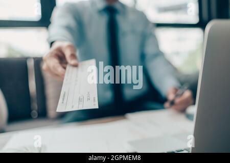 Eine Geschäftsfrau, die dem Kunden einen Scheck übergibt, und eine Rechnung, eine Münze, einen Laptop und ein Diagramm auf dem Schreibtisch im Büro. Zahlung per Scheck, Gehaltsscheck, Bezahlung Stockfoto
