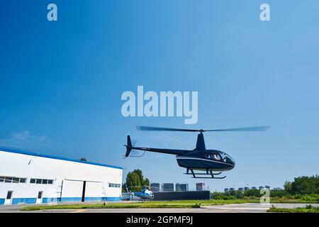 Bemannter privater Hubschrauber überfliegt den Hubschrauberlandeplatz an einem sonnigen Tag Stockfoto