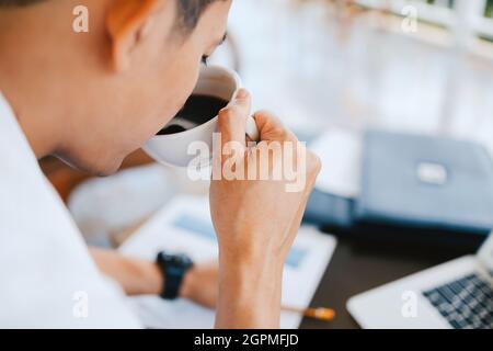 Ein Geschäftsmann hält eine Kaffeetasse in den Händen und einen Computer auf dem Tisch im Café. Junge Freiberufler trinken Kaffee und arbeiten. Stockfoto