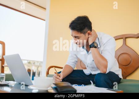 Geschäftsmann schmerzhafter Hals, während er am Sofa am Arbeitsplatz sitzt. Konzept des Office-Syndroms. Stockfoto