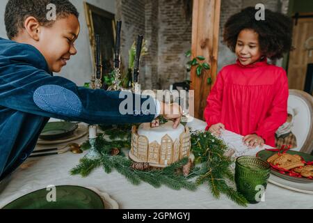 Schwester und Bruder dekorieren Lebkuchenkuchen zu Hause. Weihnachtszeit Familienfreizeitkonzept. Idee für selbstgemachte Happy New Year Süßigkeiten. Stockfoto