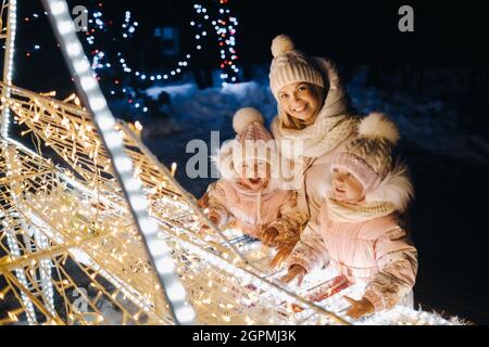 Mama und Kinder in der Abendstadt mit nächtlichen Weihnachtslichtern. Stockfoto