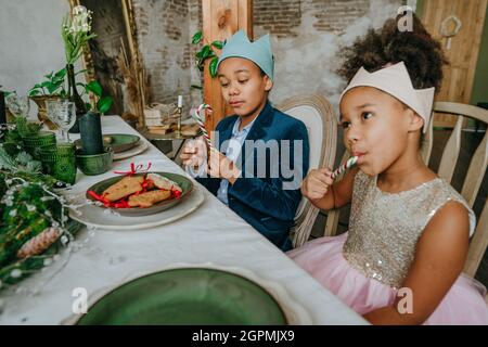 Schwester und Bruder, die Weihnachtsgeschenke essen, sitzen zu Hause am Tisch. Stockfoto