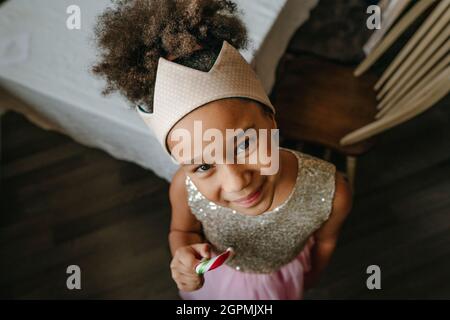 Mädchen tragen Spielzeug Krone Essen Weihnachten Candy Cane stehen in der Nähe des Tisches zu Hause. Stockfoto