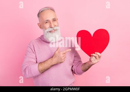 Foto von flirty optimistischen grauen Haaren gealterten Mann Punkt Herz tragen rosa Pullover auf pastellfarbenem Hintergrund isoliert Stockfoto