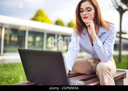Fröhliche junge Rotschopf kaukasische Frau mit Laptop im Freien im Stadtpark Stockfoto