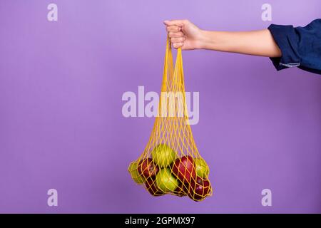 Beschnittenes Foto einer weiblichen Erd-Aktivistin empfiehlt die Verwendung eines wiederverwendbaren Zero Waste Netzbeutels, der auf violettem Hintergrund isoliert ist Stockfoto