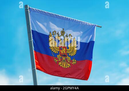 Russische Flagge mit dem Wappen, zweiköpfiger Adler ohne Schild gegen blauen Himmel Stockfoto